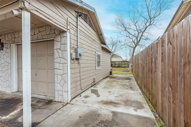 view of side of home with a patio, stone siding, and fence