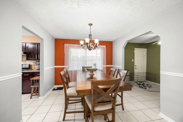 dining space featuring a textured ceiling, light tile patterned flooring, arched walkways, and an inviting chandelier