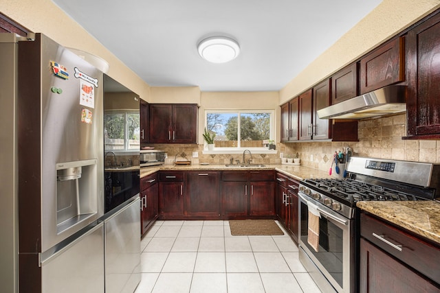 kitchen with stainless steel appliances, tasteful backsplash, a sink, light stone countertops, and under cabinet range hood