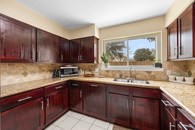 kitchen with a sink, dark brown cabinets, backsplash, light stone countertops, and stainless steel microwave