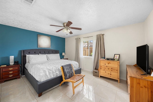 bedroom featuring light tile patterned floors, visible vents, a ceiling fan, a textured ceiling, and baseboards