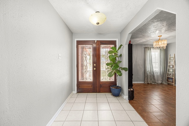 foyer entrance with a notable chandelier, a textured wall, a textured ceiling, baseboards, and tile patterned floors