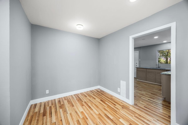 spare room featuring light wood-type flooring, a sink, baseboards, and recessed lighting