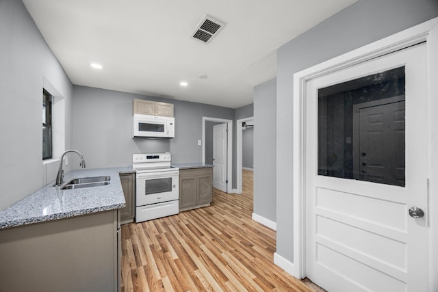 kitchen with white appliances, a sink, visible vents, baseboards, and light wood-style floors