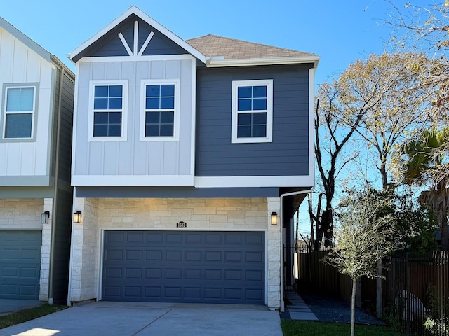 view of front of home with roof with shingles, concrete driveway, board and batten siding, fence, and stone siding