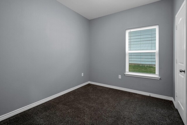 spare room with dark carpet and baseboards