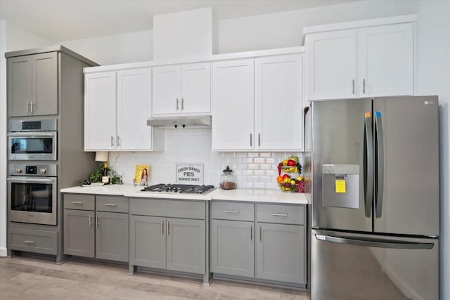 kitchen with light countertops, backsplash, gray cabinetry, appliances with stainless steel finishes, and under cabinet range hood