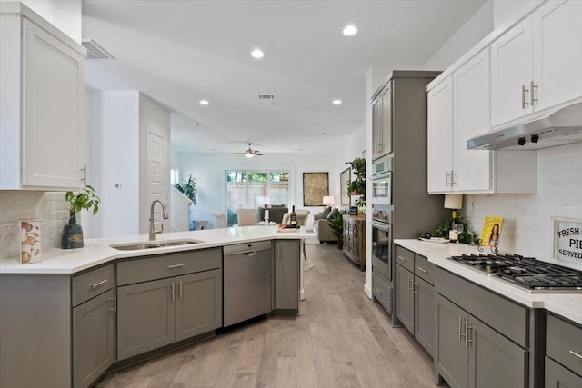 kitchen featuring visible vents, a peninsula, stainless steel appliances, gray cabinetry, and a sink