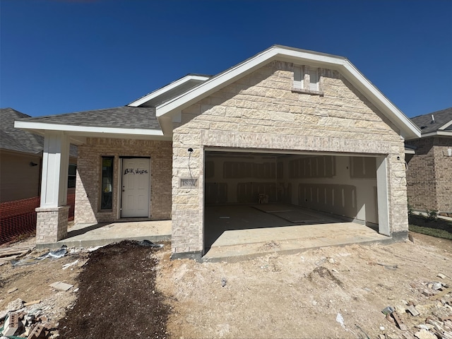 view of front of property with a garage, stone siding, and a shingled roof
