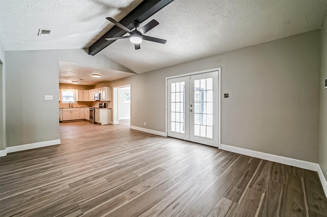 unfurnished living room featuring french doors, visible vents, light wood-style flooring, a sink, and a textured ceiling