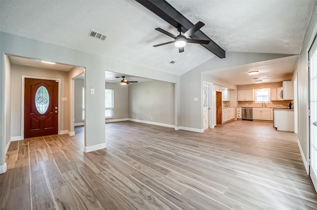 unfurnished living room featuring light wood finished floors, visible vents, lofted ceiling with beams, a textured ceiling, and baseboards