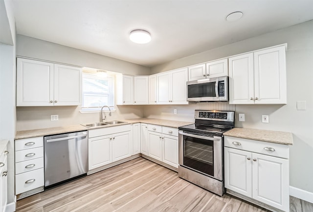 kitchen with appliances with stainless steel finishes, white cabinetry, a sink, and light wood finished floors