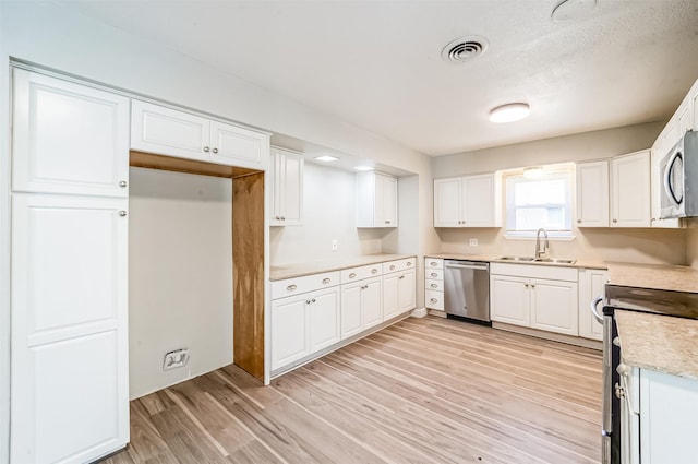 kitchen featuring light wood finished floors, visible vents, appliances with stainless steel finishes, white cabinets, and a sink