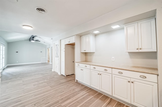 kitchen with lofted ceiling, white cabinetry, visible vents, light wood-style floors, and light countertops