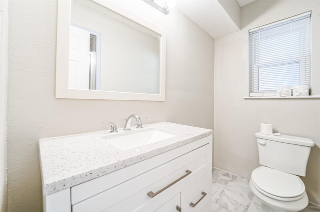 half bath with toilet, marble finish floor, and vanity