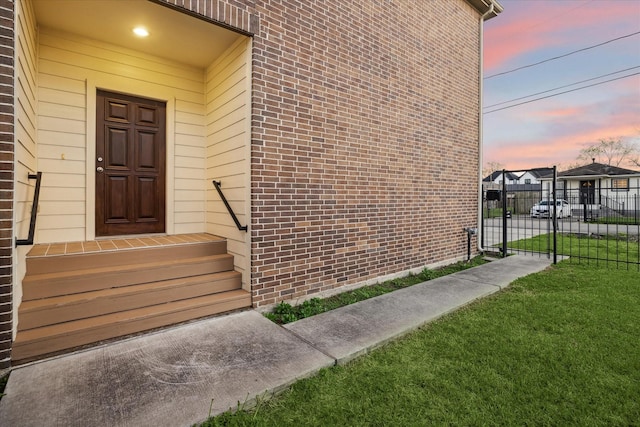 doorway to property featuring a gate, a lawn, brick siding, and fence