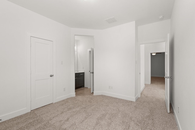 unfurnished bedroom featuring light carpet, ensuite bath, visible vents, and baseboards