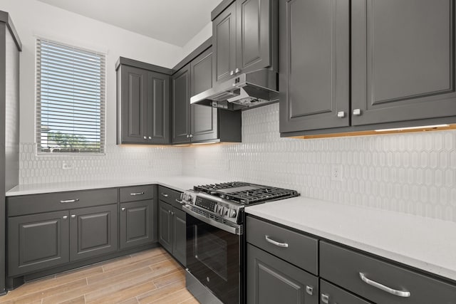 kitchen with light countertops, backsplash, gray cabinetry, stainless steel gas range, and under cabinet range hood