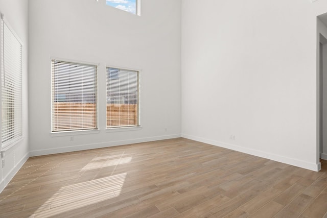 spare room with light wood-type flooring, a towering ceiling, and baseboards