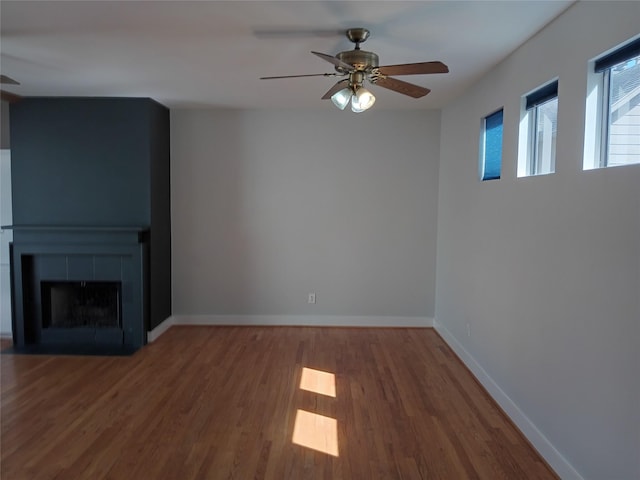 unfurnished living room with a ceiling fan, a fireplace, baseboards, and wood finished floors