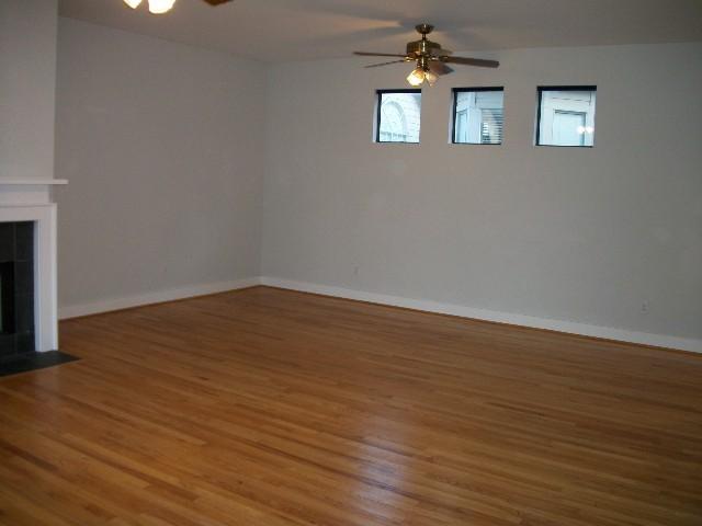 unfurnished living room featuring a ceiling fan, a fireplace, baseboards, and wood finished floors