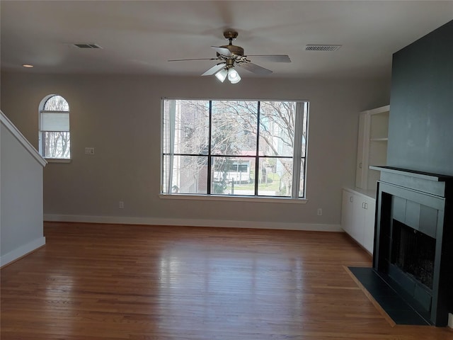 unfurnished living room featuring wood finished floors, a tile fireplace, visible vents, and baseboards