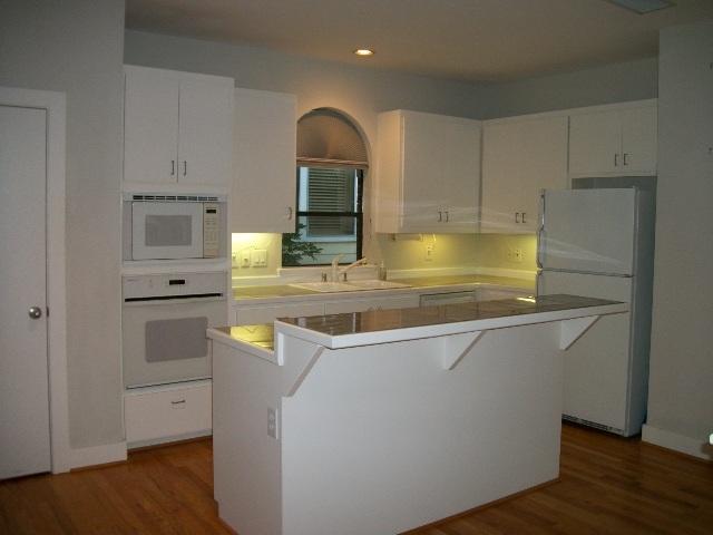 kitchen with dark wood finished floors, white appliances, white cabinetry, and a sink