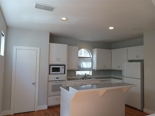 kitchen with white appliances, visible vents, white cabinets, a kitchen island, and a sink