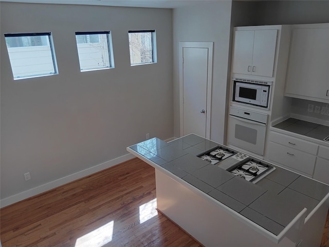 kitchen featuring tile counters, light wood-style floors, white cabinets, white appliances, and baseboards