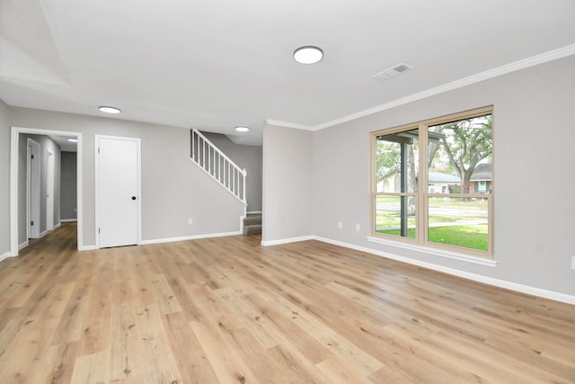 empty room with ornamental molding, light wood-style flooring, baseboards, and stairs