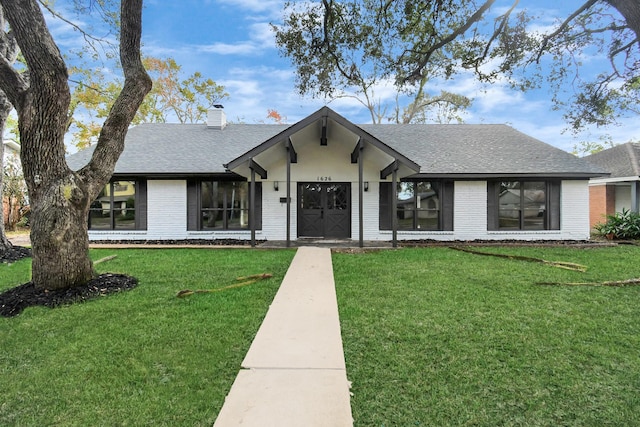 view of front of home featuring an attached garage, brick siding, a shingled roof, a chimney, and a front yard