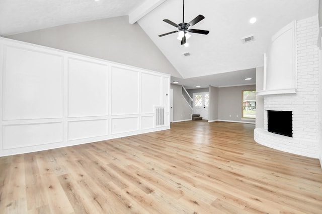 unfurnished living room with visible vents, stairway, a brick fireplace, a decorative wall, and beam ceiling