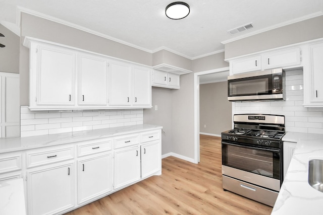 kitchen with light stone counters, visible vents, light wood-style flooring, appliances with stainless steel finishes, and white cabinetry