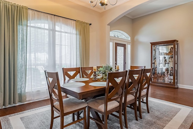 dining area featuring baseboards, arched walkways, wood finished floors, an inviting chandelier, and crown molding