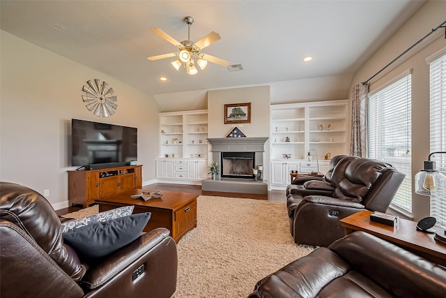 living area featuring wood finished floors, visible vents, baseboards, a ceiling fan, and a glass covered fireplace