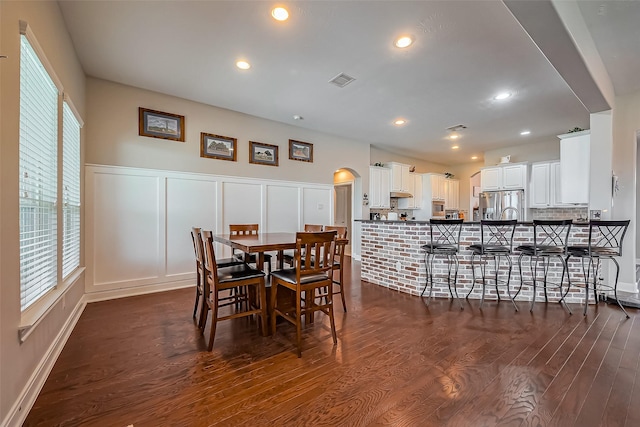 dining area featuring a healthy amount of sunlight, visible vents, a decorative wall, and dark wood finished floors