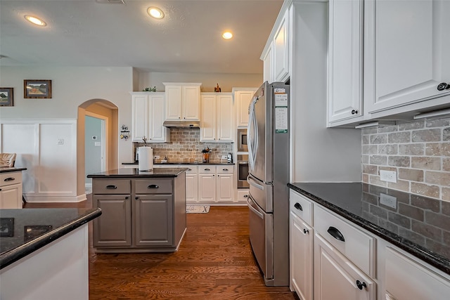 kitchen featuring arched walkways, under cabinet range hood, white cabinets, appliances with stainless steel finishes, and dark wood-style floors