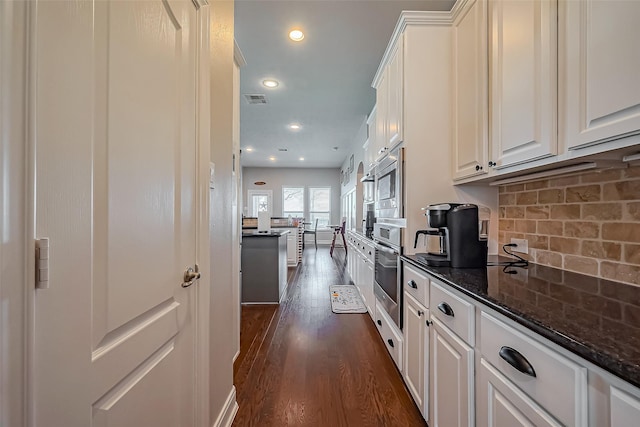 kitchen featuring stainless steel oven, visible vents, white cabinets, tasteful backsplash, and dark wood finished floors