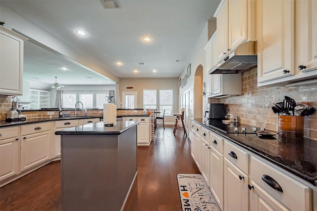 kitchen with black electric stovetop, under cabinet range hood, a peninsula, a sink, and dark wood-style floors