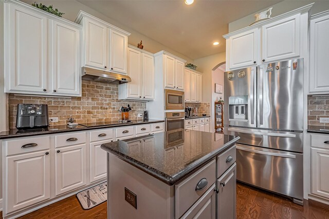 kitchen with appliances with stainless steel finishes, arched walkways, dark wood-style flooring, and under cabinet range hood