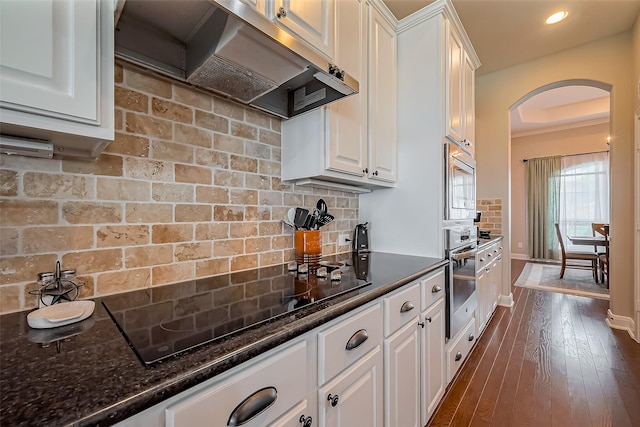 kitchen with arched walkways, under cabinet range hood, stainless steel appliances, white cabinets, and decorative backsplash