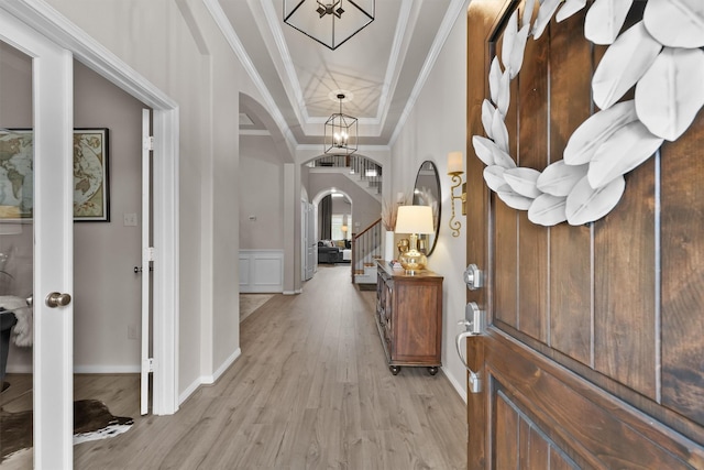 foyer featuring a tray ceiling, arched walkways, ornamental molding, stairs, and light wood-type flooring