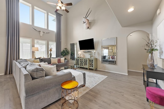 living room with a ceiling fan, wood finished floors, baseboards, a high ceiling, and arched walkways