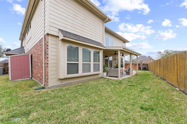 back of house featuring a ceiling fan, a fenced backyard, brick siding, and a lawn