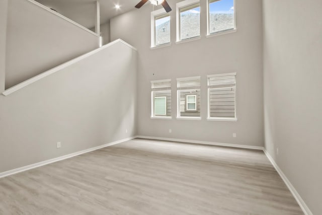 unfurnished living room featuring ceiling fan, a towering ceiling, wood finished floors, and baseboards