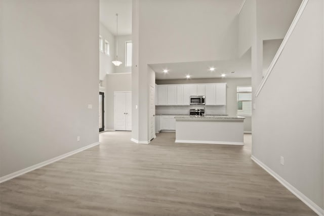 unfurnished living room with baseboards, light wood-type flooring, and a high ceiling