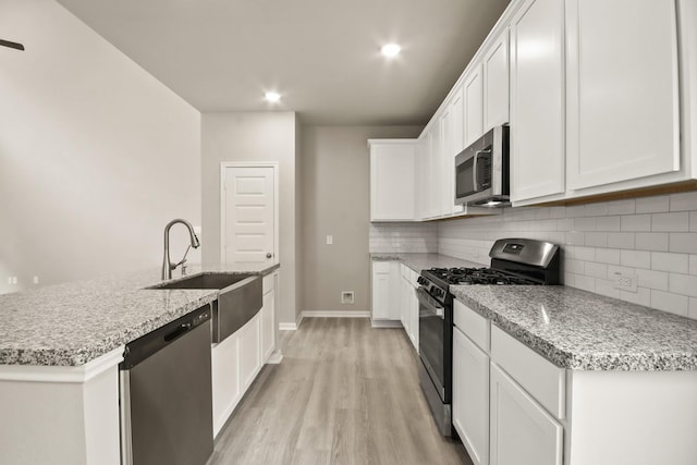 kitchen with tasteful backsplash, white cabinets, a sink, appliances with stainless steel finishes, and light wood finished floors