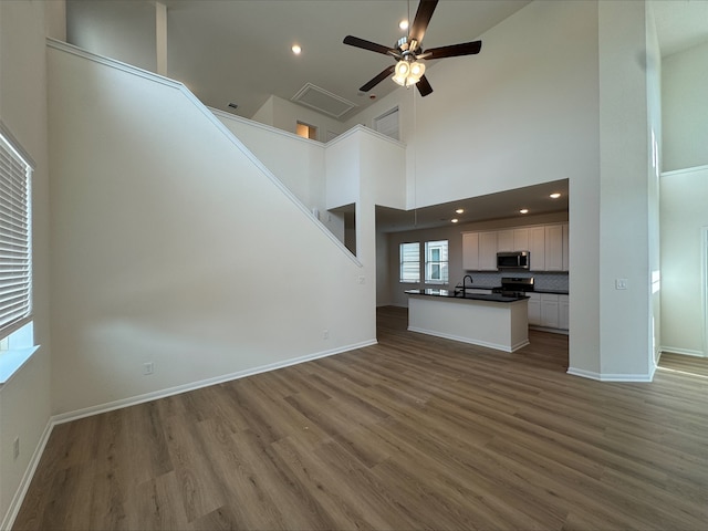 18757 Lucas Michael Way, New Caney, TX 77357 - unfurnished living room featuring a ceiling fan, wood finished floors, a sink, a high ceiling, and baseboards