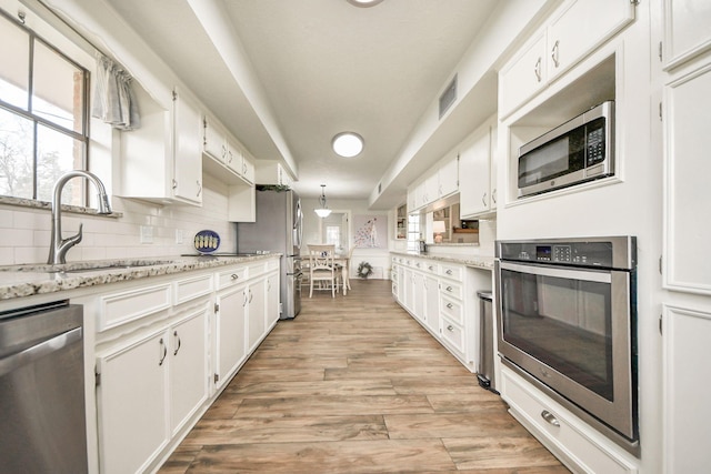 kitchen featuring backsplash, light wood-style flooring, appliances with stainless steel finishes, white cabinets, and a sink