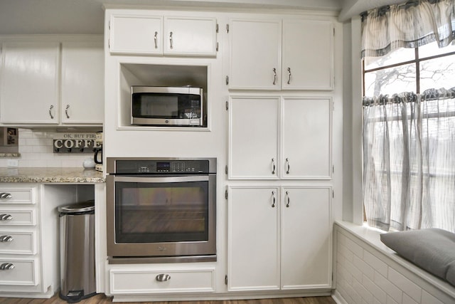 kitchen featuring backsplash, white cabinetry, stainless steel appliances, and light stone countertops